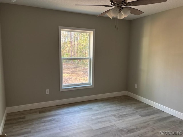 spare room with ceiling fan, a textured ceiling, baseboards, and wood finished floors