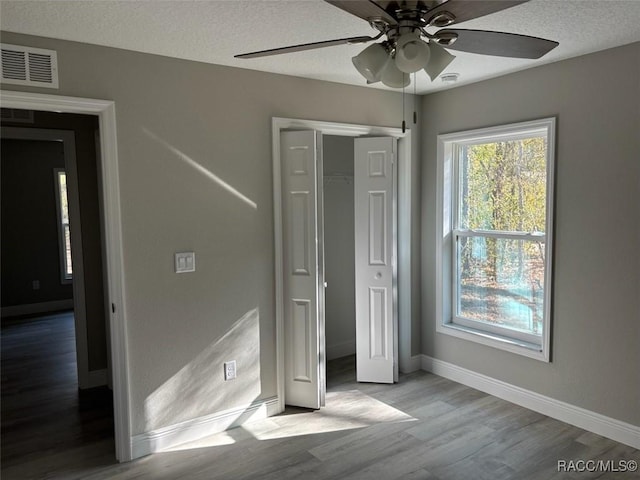 unfurnished bedroom with visible vents, a textured ceiling, baseboards, and wood finished floors