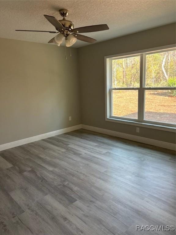 empty room with baseboards, a textured ceiling, wood finished floors, and a ceiling fan