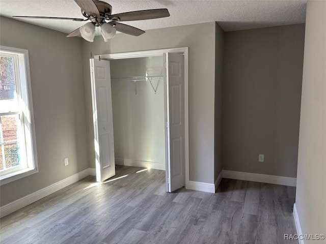 unfurnished bedroom featuring multiple windows, wood finished floors, baseboards, and a textured ceiling