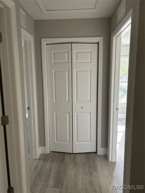 hall with light wood-type flooring, baseboards, visible vents, and attic access