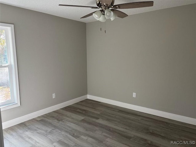 empty room featuring a textured ceiling, dark wood-type flooring, and baseboards