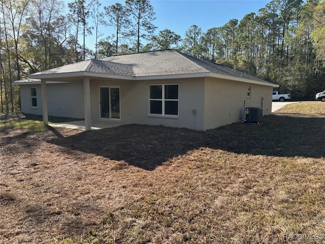 back of property featuring a yard, stucco siding, a shingled roof, and central AC