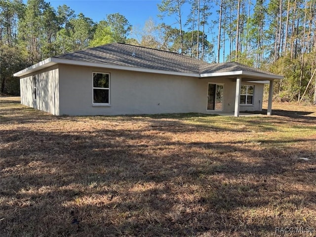 back of house featuring a lawn, roof with shingles, and stucco siding