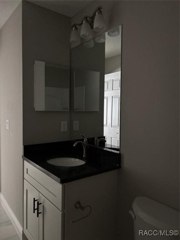 half bath featuring baseboards, toilet, and vanity