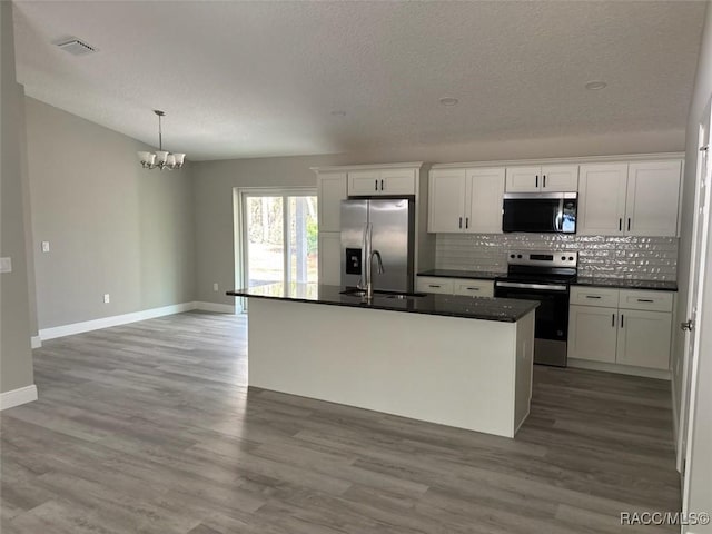 kitchen with wood finished floors, a sink, decorative backsplash, stainless steel appliances, and dark countertops