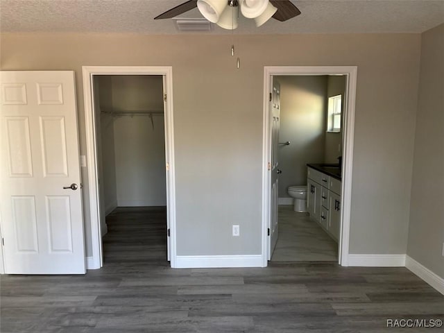 unfurnished bedroom featuring a walk in closet, ensuite bathroom, a textured ceiling, wood finished floors, and a closet