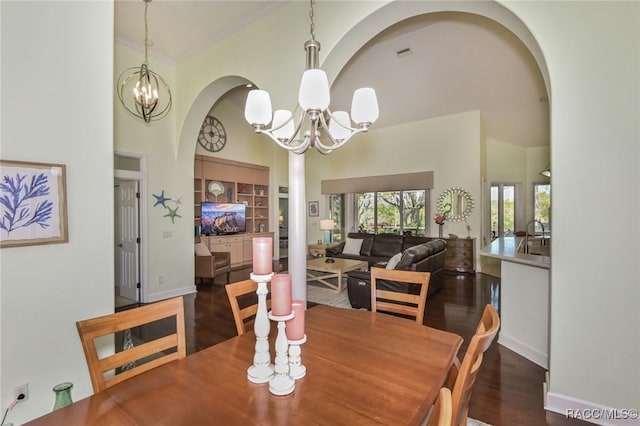 dining room with crown molding, an inviting chandelier, a towering ceiling, dark hardwood / wood-style flooring, and built in shelves