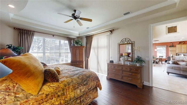 bedroom with multiple windows, a tray ceiling, hardwood / wood-style flooring, and visible vents