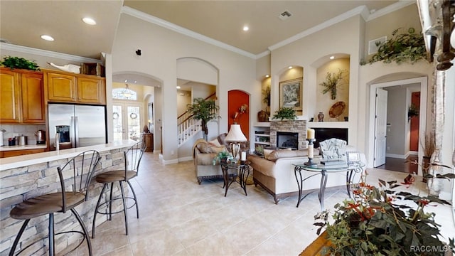 living room featuring a high ceiling, a fireplace, visible vents, baseboards, and crown molding