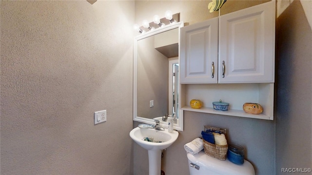 half bath with toilet, a sink, and a textured wall