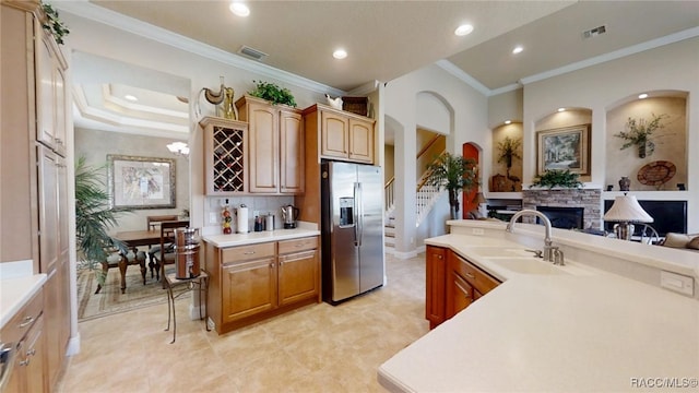 kitchen with light countertops, crown molding, a fireplace, stainless steel refrigerator with ice dispenser, and a sink