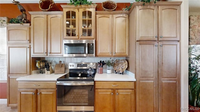 kitchen with light countertops, appliances with stainless steel finishes, backsplash, and glass insert cabinets