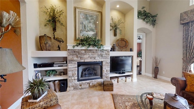 tiled living area featuring a fireplace, a ceiling fan, and baseboards