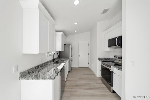 kitchen featuring lofted ceiling, sink, appliances with stainless steel finishes, light stone counters, and white cabinetry