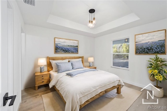 bedroom featuring visible vents, a tray ceiling, light wood-style flooring, and baseboards