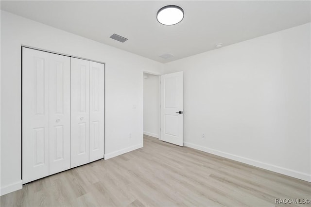 unfurnished bedroom with visible vents, a closet, light wood-style flooring, and baseboards