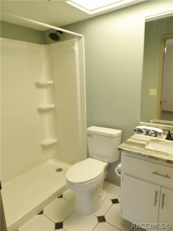 bathroom featuring tile patterned flooring, vanity, toilet, and walk in shower