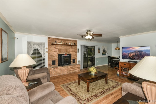 living room with ceiling fan, wood-type flooring, crown molding, and a wood stove