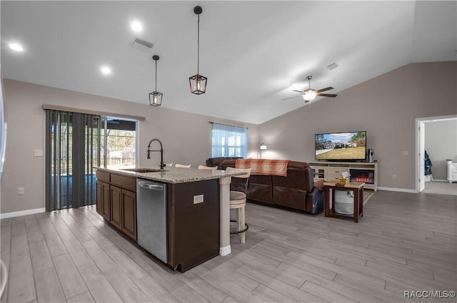 kitchen featuring sink, light stone counters, hanging light fixtures, dishwasher, and an island with sink