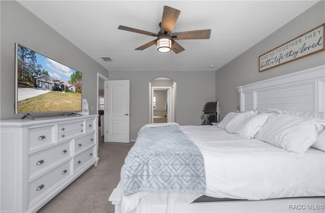 bedroom with ensuite bathroom, light colored carpet, and ceiling fan