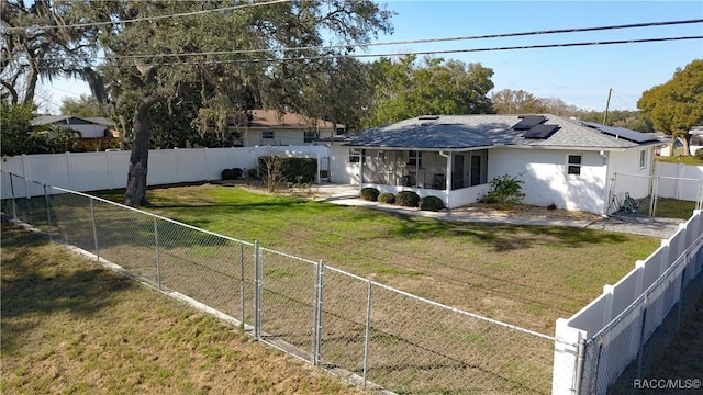 rear view of house with a yard, a sunroom, and solar panels