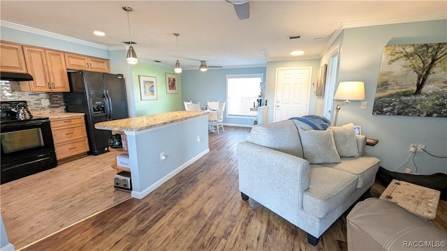 kitchen featuring hardwood / wood-style flooring, ornamental molding, black appliances, a kitchen island, and decorative backsplash