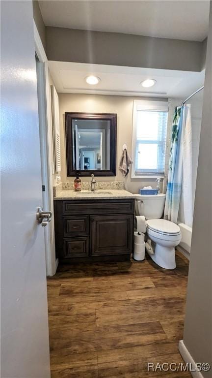 full bathroom featuring hardwood / wood-style flooring, vanity, shower / bath combination with curtain, and toilet