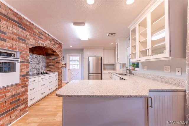 kitchen with kitchen peninsula, wall oven, a textured ceiling, white cabinets, and stainless steel refrigerator