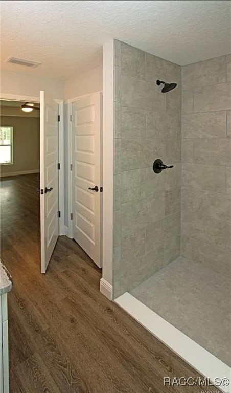 bathroom featuring wood-type flooring, a textured ceiling, and a tile shower