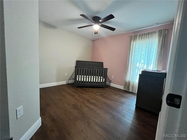 bedroom with ceiling fan, a nursery area, and dark hardwood / wood-style floors