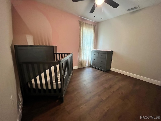 bedroom featuring ceiling fan, dark wood-type flooring, and a nursery area