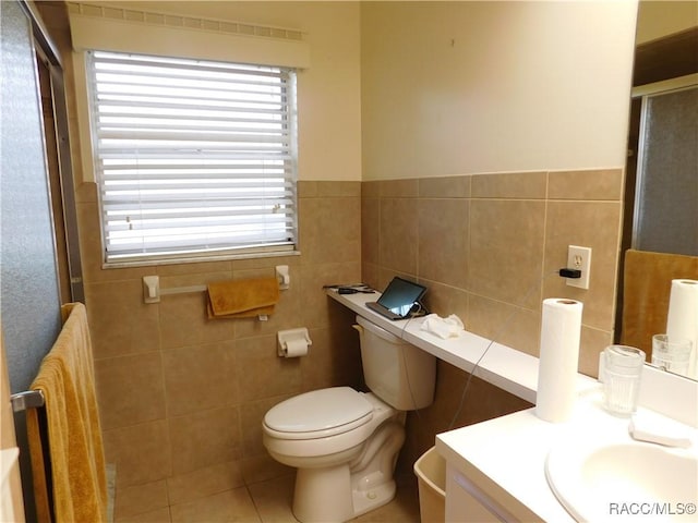 bathroom featuring tile patterned flooring, tile walls, vanity, toilet, and walk in shower