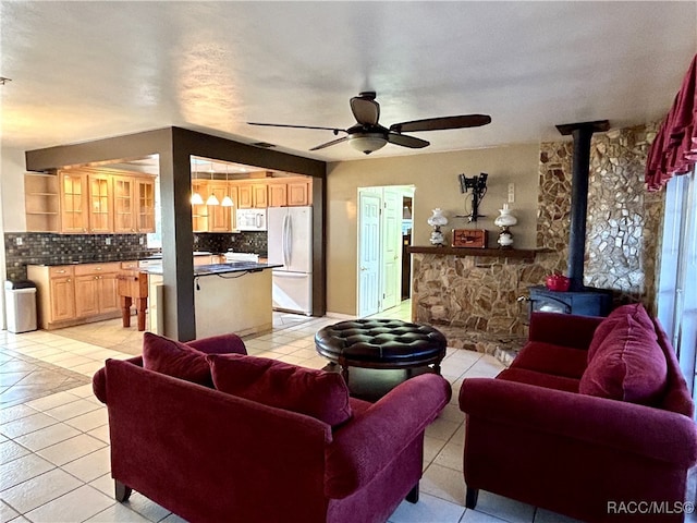 living room with a textured ceiling, a wood stove, ceiling fan, and light tile patterned flooring