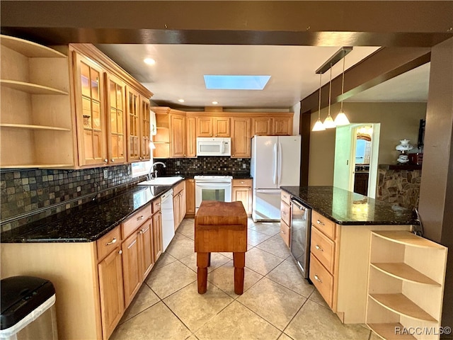 kitchen with white appliances, backsplash, dark stone counters, sink, and a skylight