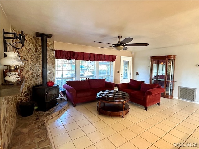 living room with ceiling fan, a wood stove, and light tile patterned floors