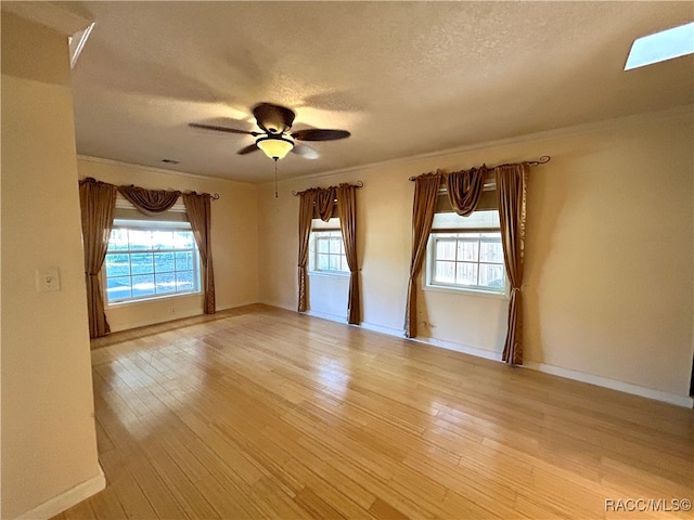 empty room with a skylight, light hardwood / wood-style flooring, a wealth of natural light, and ceiling fan