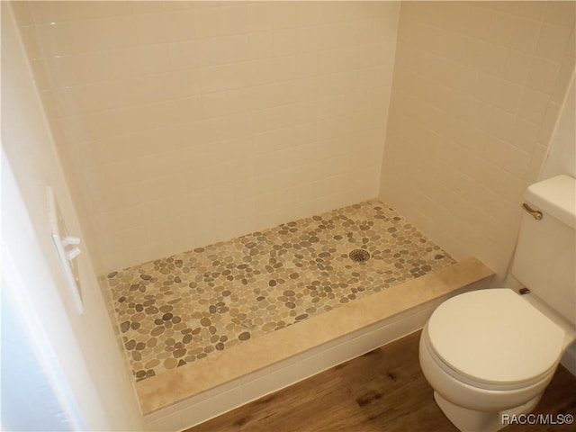 bathroom with wood-type flooring, tiled shower, and toilet