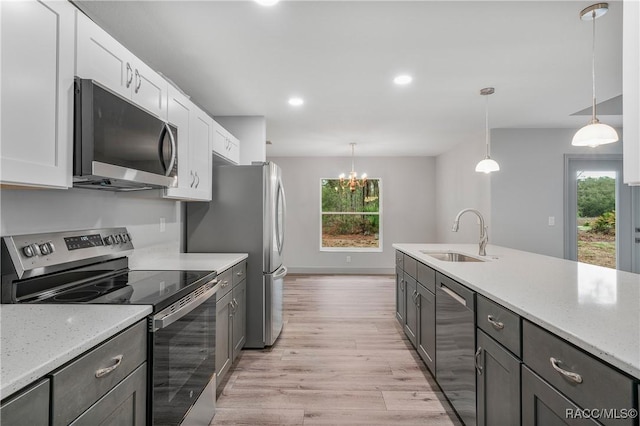 kitchen with white cabinets, light wood-style flooring, light stone counters, stainless steel appliances, and a sink