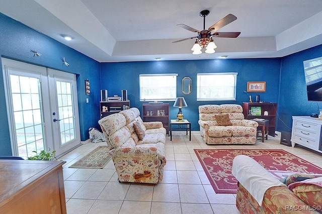 living area with a healthy amount of sunlight, a ceiling fan, light tile patterned flooring, and a tray ceiling