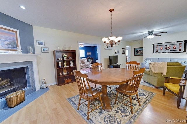 dining room with a fireplace with flush hearth, baseboards, ceiling fan with notable chandelier, and light wood finished floors