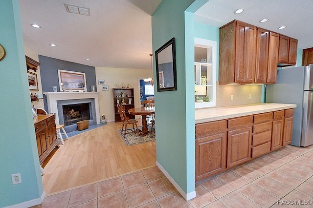 kitchen featuring visible vents, a fireplace with flush hearth, freestanding refrigerator, tile counters, and light tile patterned flooring