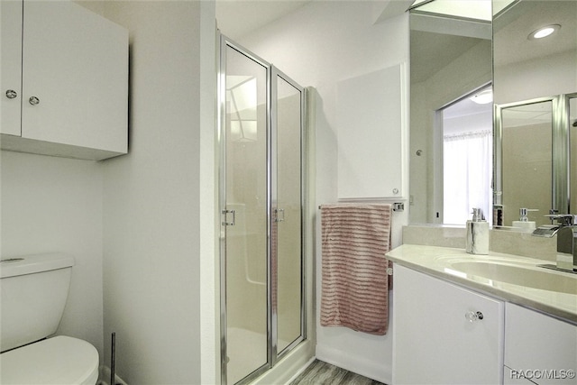 bathroom featuring wood-type flooring, vanity, toilet, and a shower with door