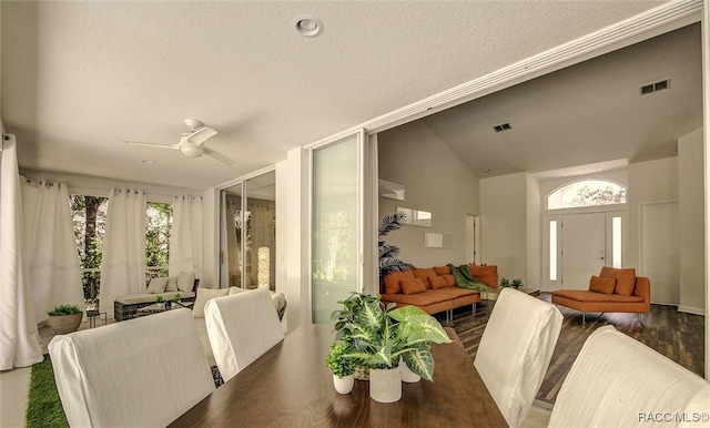 dining area with a textured ceiling, ceiling fan, dark wood-type flooring, and vaulted ceiling