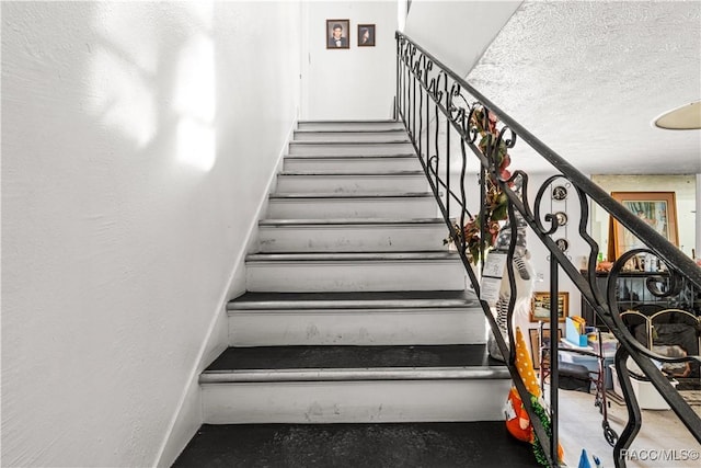 stairway with a textured ceiling, a textured wall, and baseboards