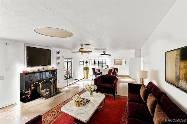 living room with wood-type flooring, a textured ceiling, ceiling fan, and a tiled fireplace