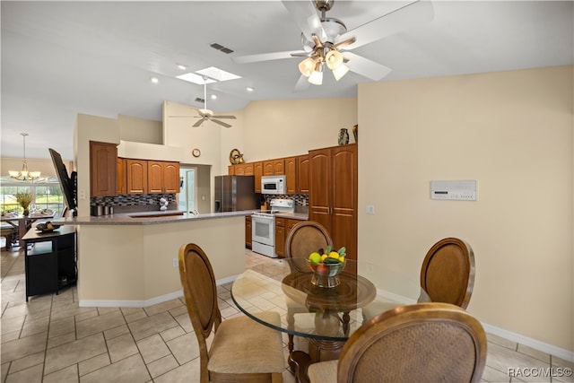 tiled dining space with ceiling fan with notable chandelier, a skylight, and high vaulted ceiling