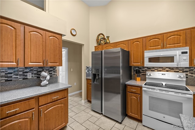 kitchen featuring tasteful backsplash, light tile patterned floors, a high ceiling, and white appliances