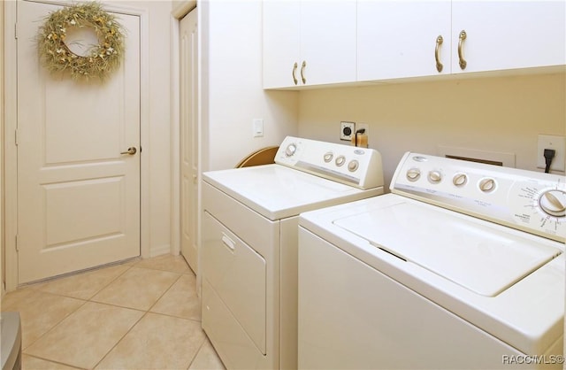 washroom featuring washing machine and clothes dryer, light tile patterned flooring, and cabinets