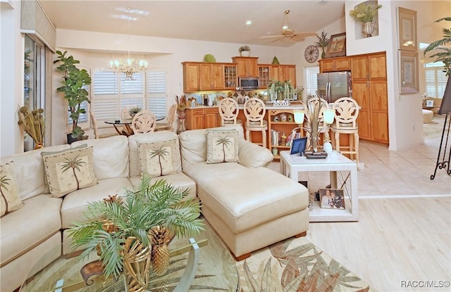 living room with ceiling fan with notable chandelier, light hardwood / wood-style floors, and lofted ceiling